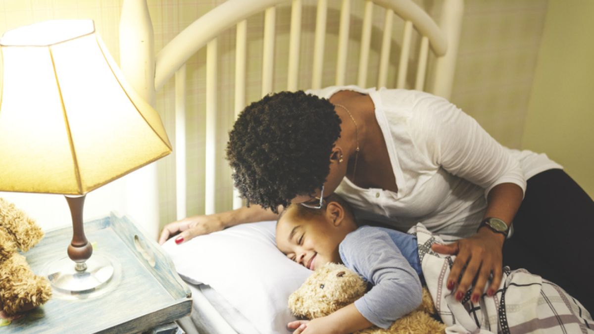 Mother putting child to bed with teddy bear