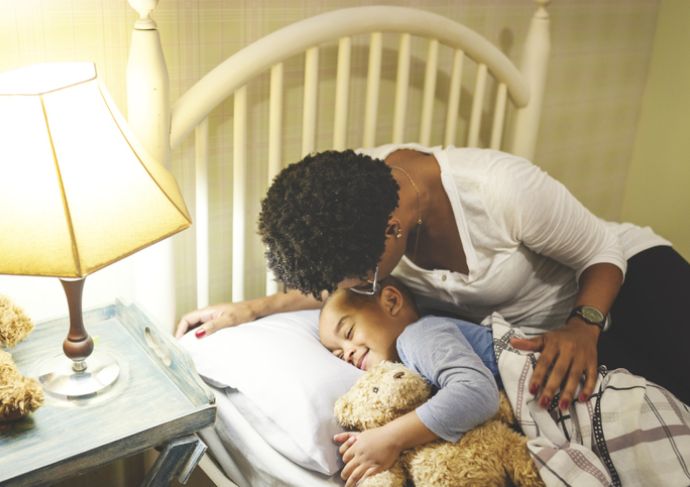 Mother putting child to bed with teddy bear