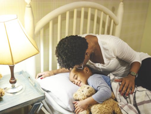 Mother putting child to bed with teddy bear
