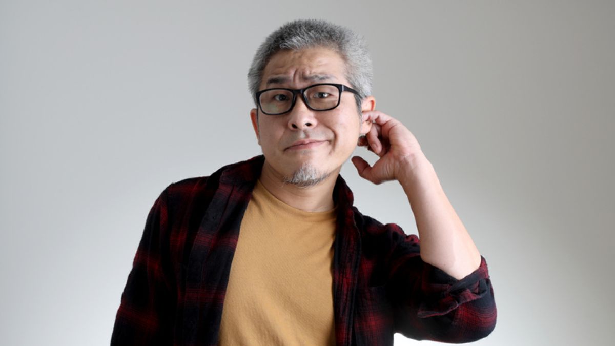 Man with glasses and gray hair scratches ear with his finger