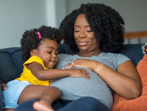Pregnant woman sitting on the couch with her daughter