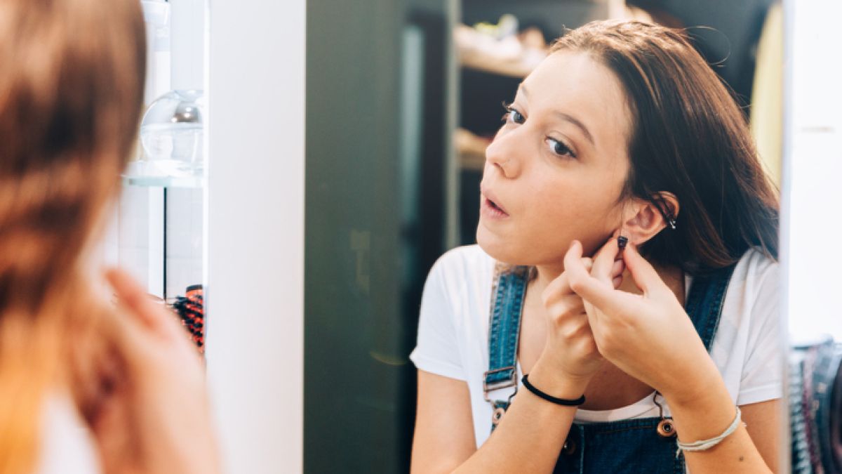 Girl looking in the mirror at her ear piercing