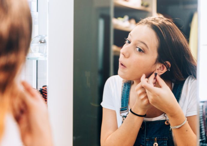 Girl looking in the mirror at her ear piercing