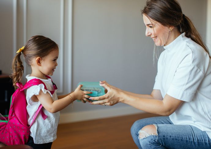 Mom putting lunch box with healthy food in kids backpack