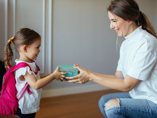 Mom putting lunch box with healthy food in kids backpack