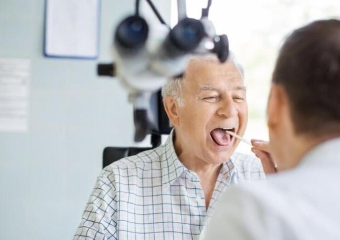 Patient sitting in a chair, having their throat looked at by a doctor
