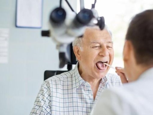 Patient sitting in a chair, having their throat looked at by a doctor