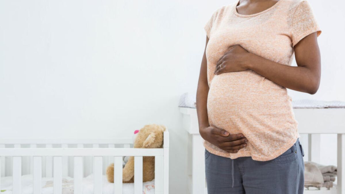 Pregnant mother standing in a nursery, holding her baby bump