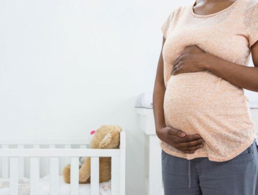 Pregnant mother standing in a nursery, holding her baby bump