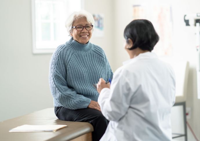 Older adult woman sitting on a clinic exam table while being seen by a female physician