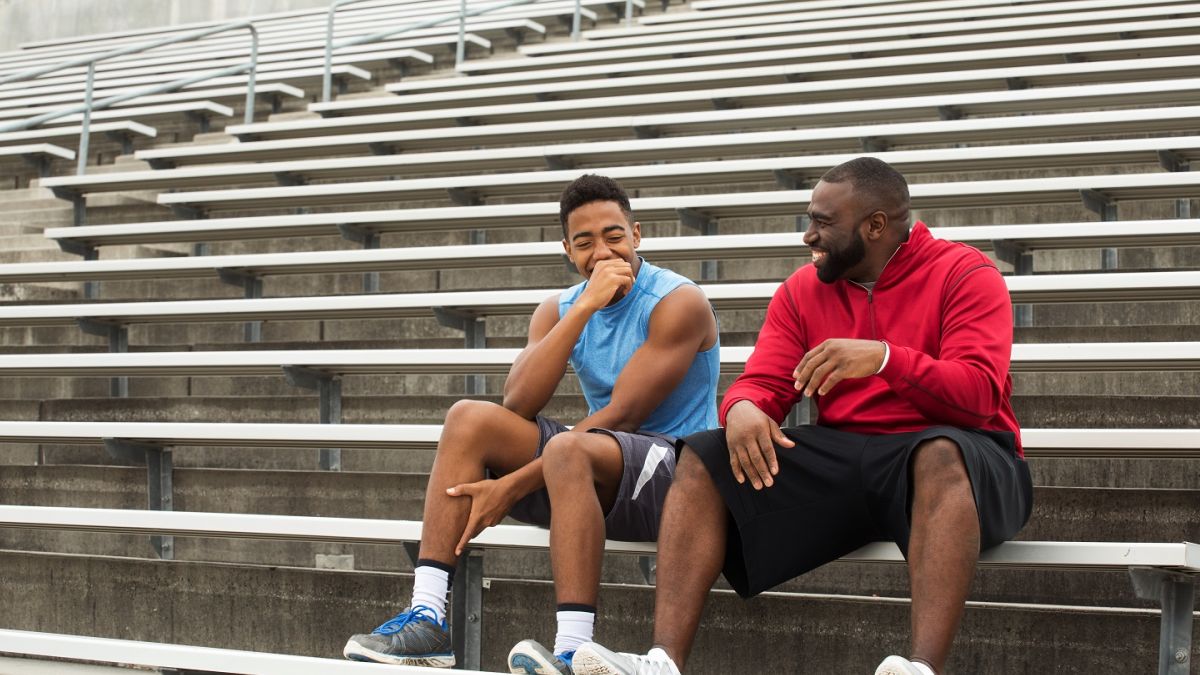 Male athletic trainer sitting with student athlete on bleachers outdoors