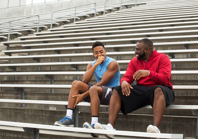 Male athletic trainer sitting with student athlete on bleachers outdoors