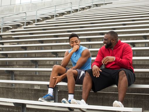 Male athletic trainer sitting with student athlete on bleachers outdoors