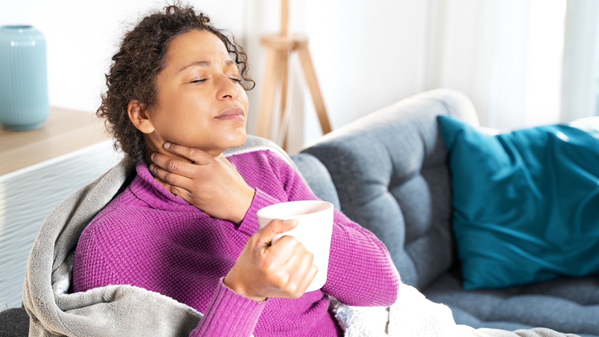 Women holding her sore throat while drinking a cup of tea