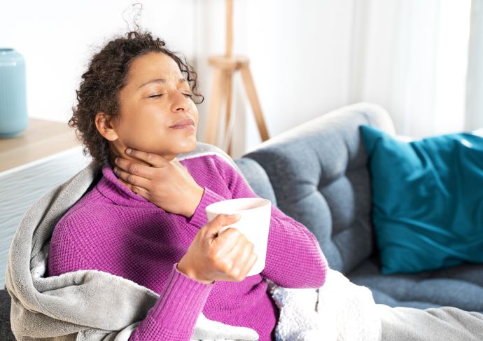 Women holding her sore throat while drinking a cup of tea