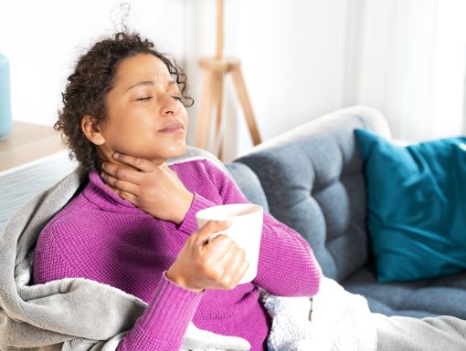 Women holding her sore throat while drinking a cup of tea