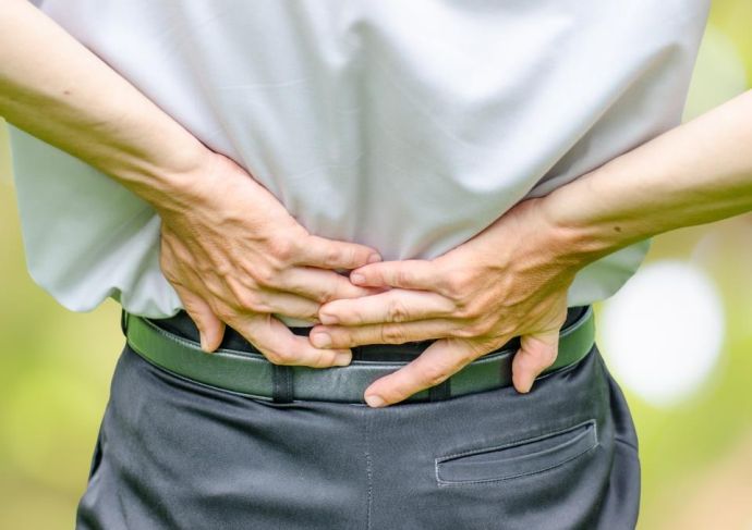 man suffering from spinal stenosis grabbing lower back in pain