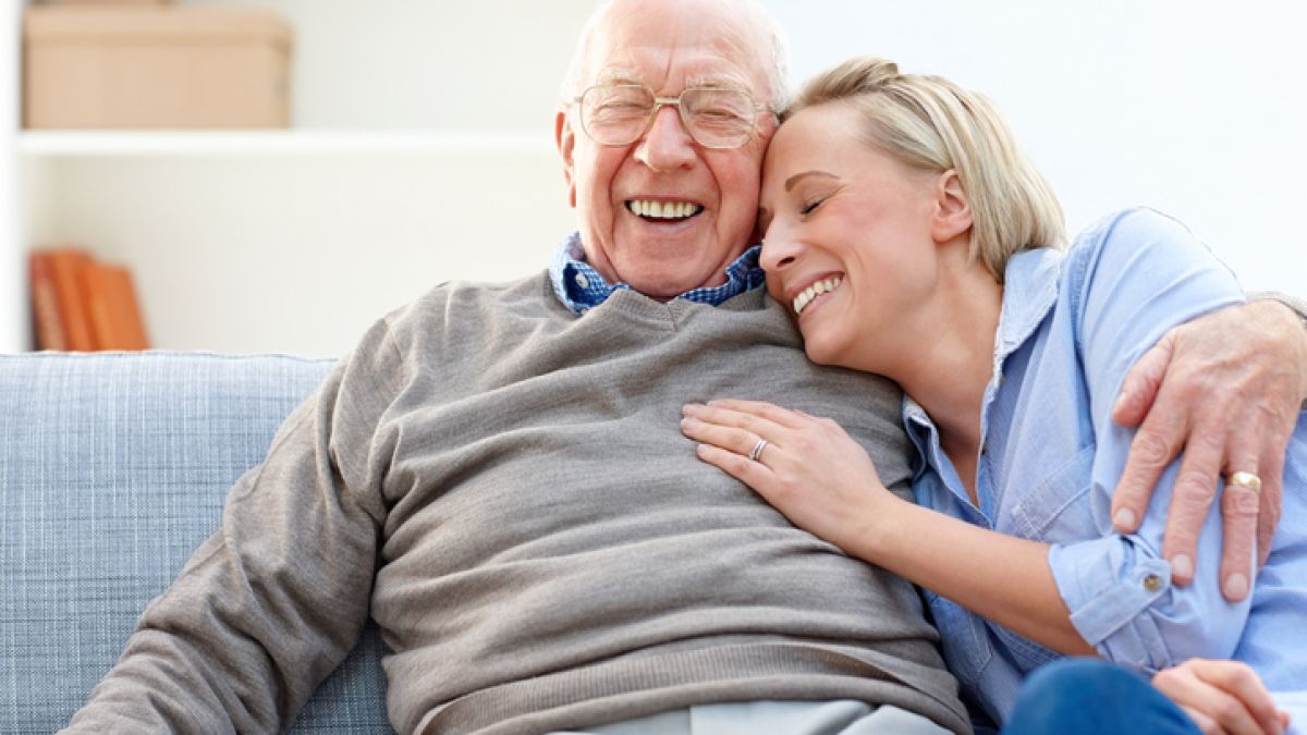 older man and woman hugging on couch smiling