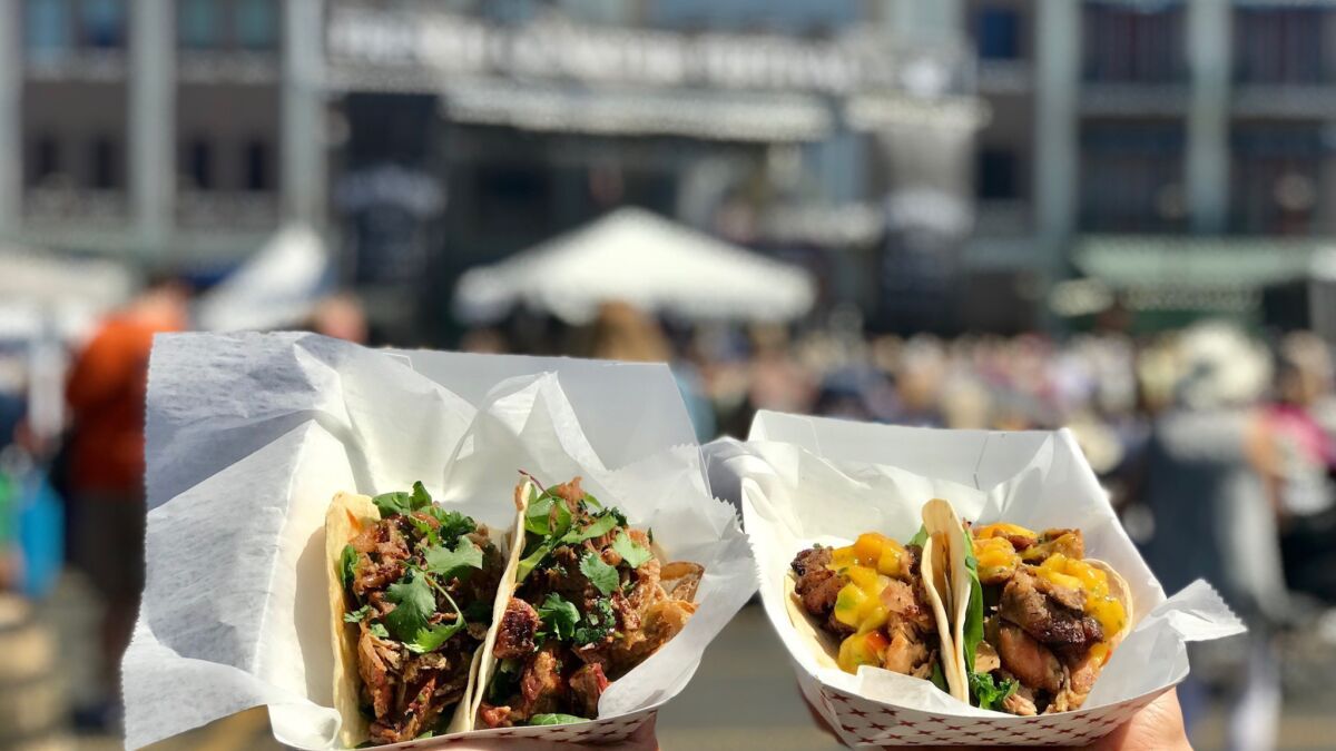 two hands holding healthy tacos at a festival