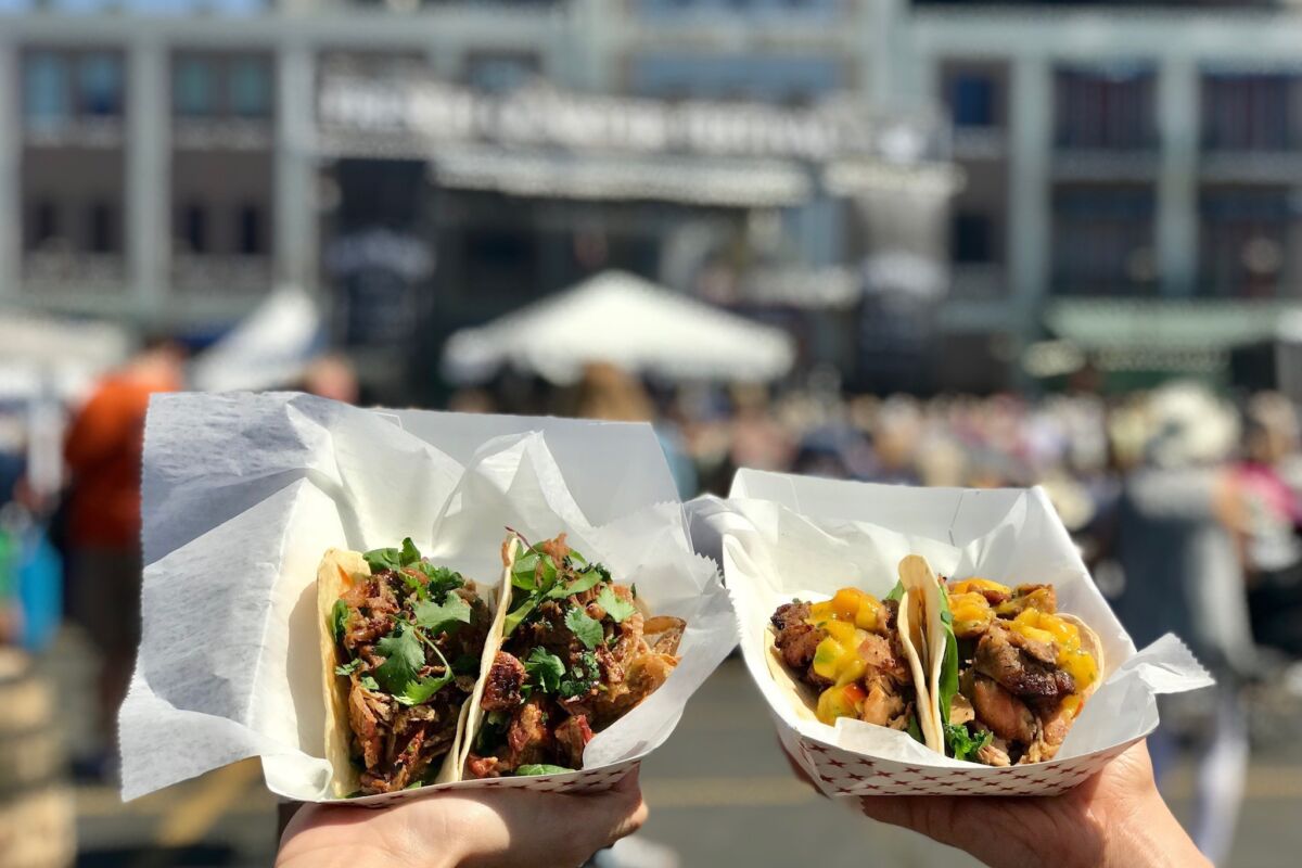 two hands holding healthy tacos at a festival
