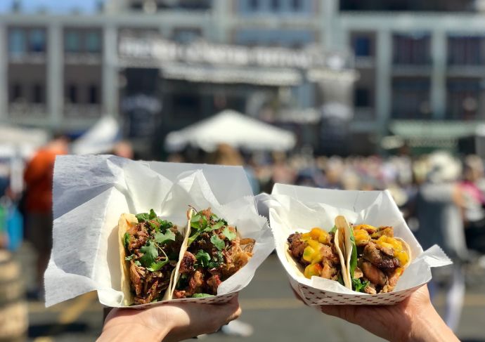 two hands holding healthy tacos at a festival