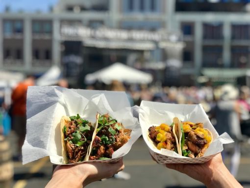 two hands holding healthy tacos at a festival