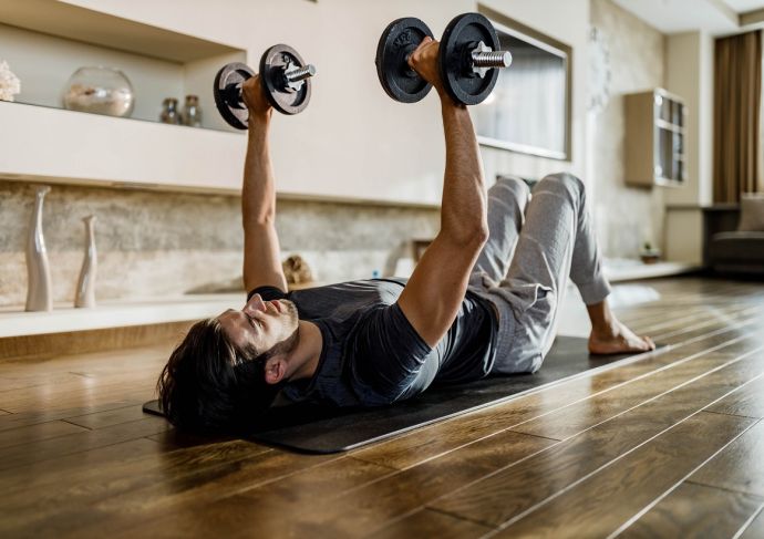 Muscular build man exercising strength with weights on a floor