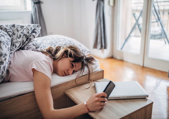 Sleepy woman checking phone in bed