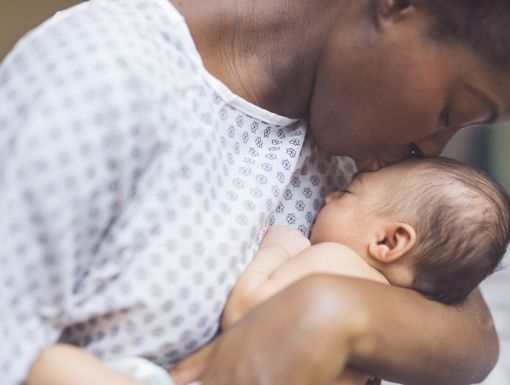 mother in hospital gown kissing newborn