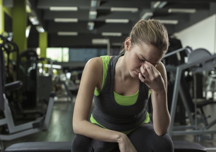 Woman at gym with head down pinching nose looking like she is not feeling well
