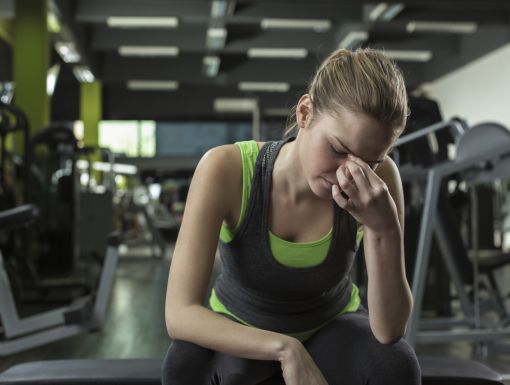 Woman at gym with head down pinching nose looking like she is not feeling well