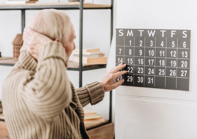 Man with grey hair touching wall calendar and head