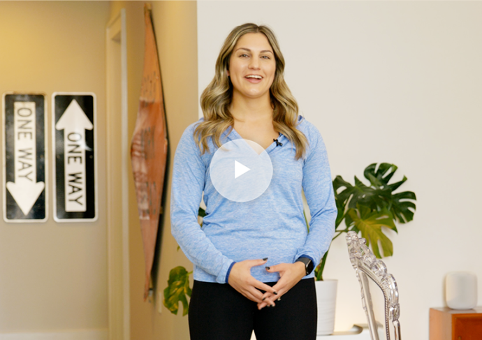Woman standing indoors talking at camera with play button