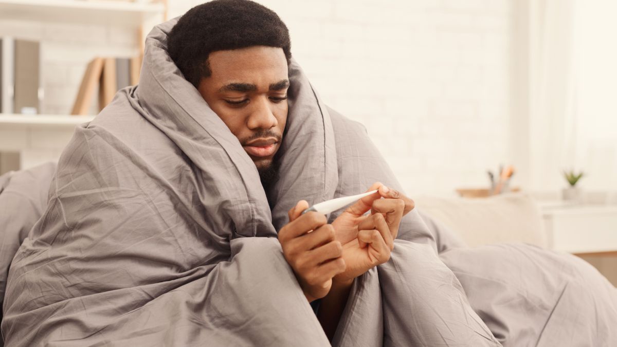 Man under duvet looking at thermometer