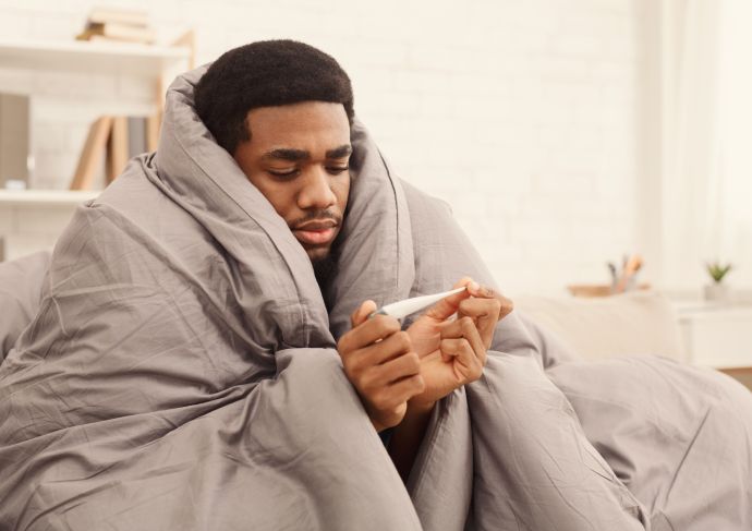 Man under duvet looking at thermometer