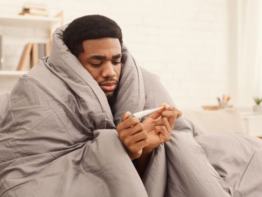Man under duvet looking at thermometer