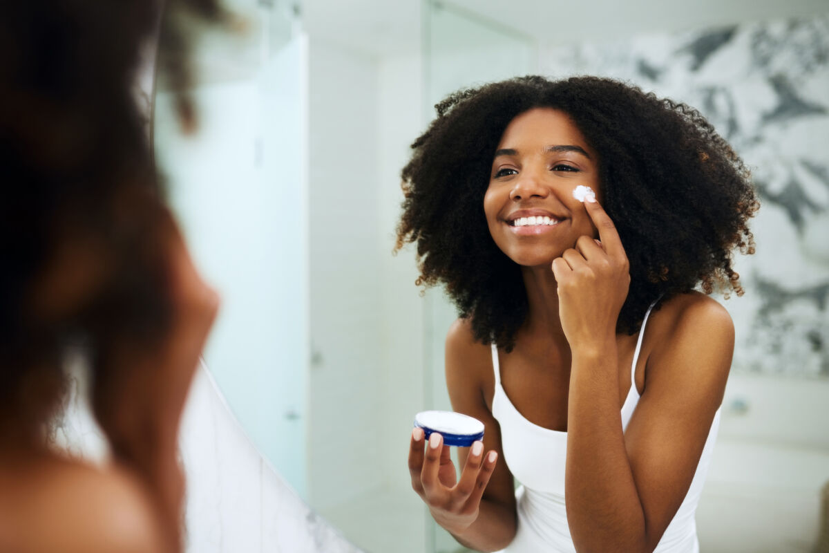 Girl looking in the mirror applying skincare lotion.
