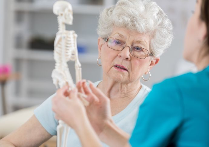 A female provider showing an elderly woman a skeleton model to showcase what happens to bones when you have osteoporosis