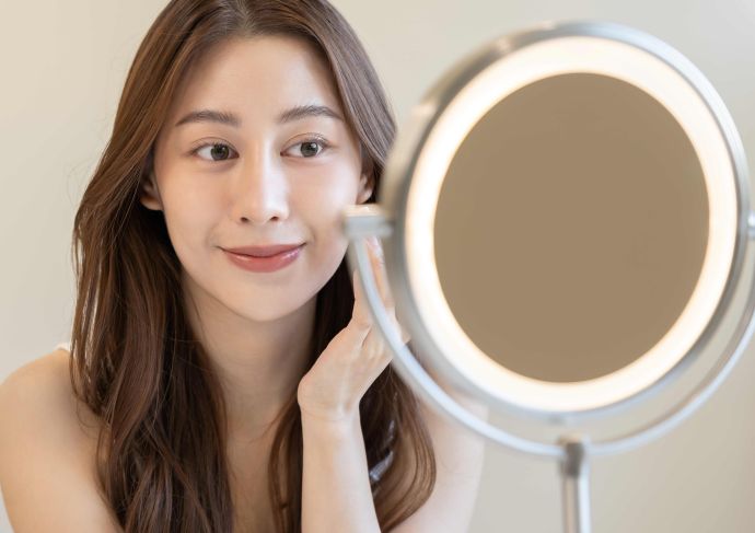 Woman looking in mirror at smooth skin after dermaplaning session