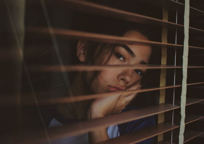 Young woman with depression looking through blinds on window