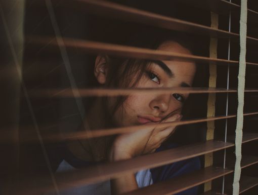 Young woman with depression looking through blinds on window