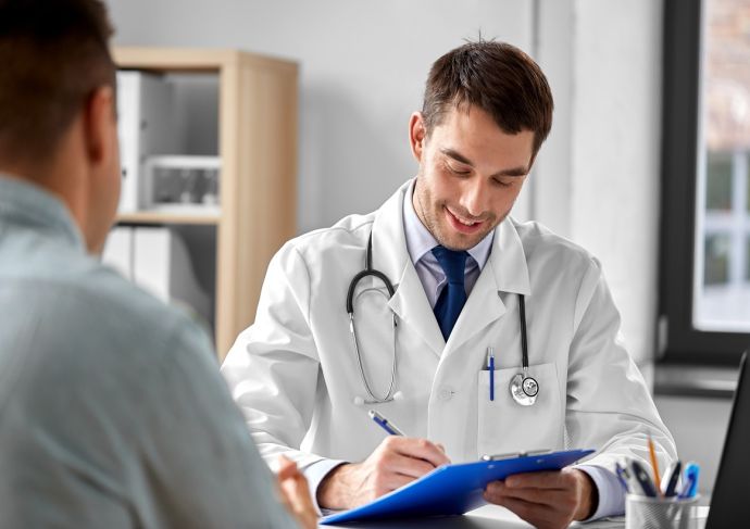 Doctor with clipboard talking to male patient at medical office in hospital