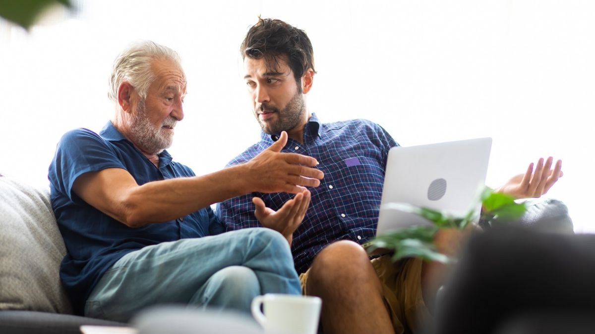 Smiling old father and happy son sitting on sofa using laptop in living room