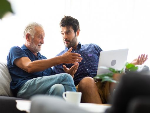 Smiling old father and happy son sitting on sofa using laptop in living room