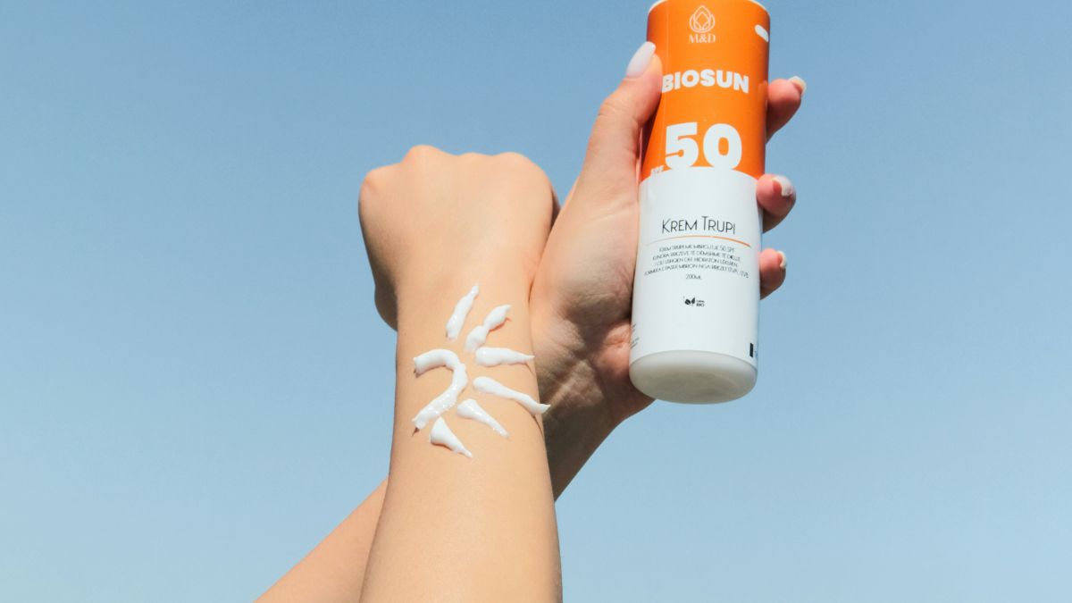 Two arms outstretched and one hand holding sunscreen bottle