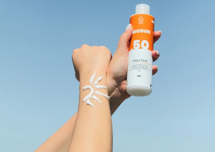 Two arms outstretched and one hand holding sunscreen bottle