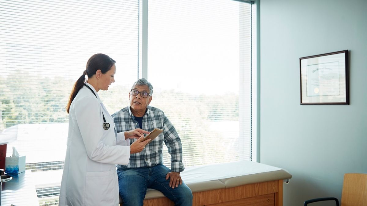 Woman doctor talking to older man in exam room