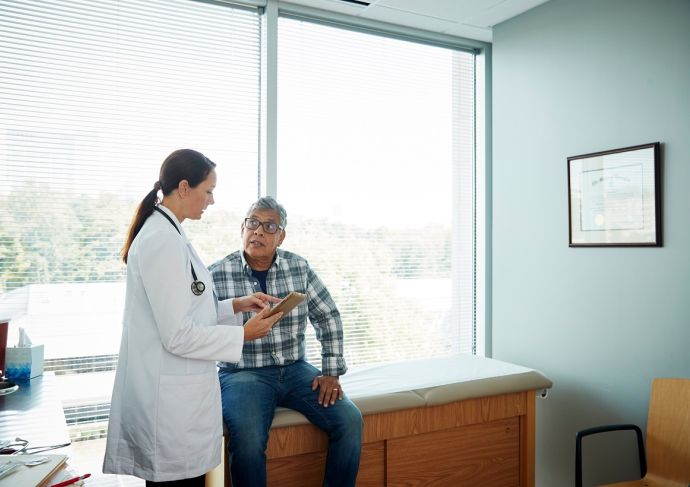 Woman doctor talking to older man in exam room