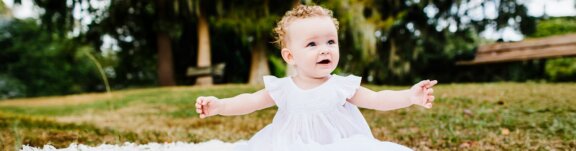 Baby in white dress sitting on grass