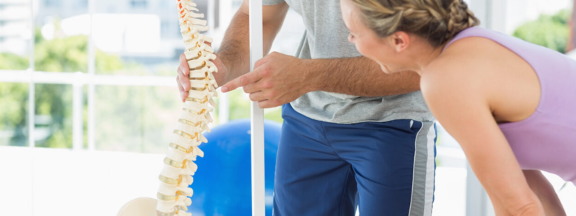 Orthopedic physical therapist shows patient a model of the spine